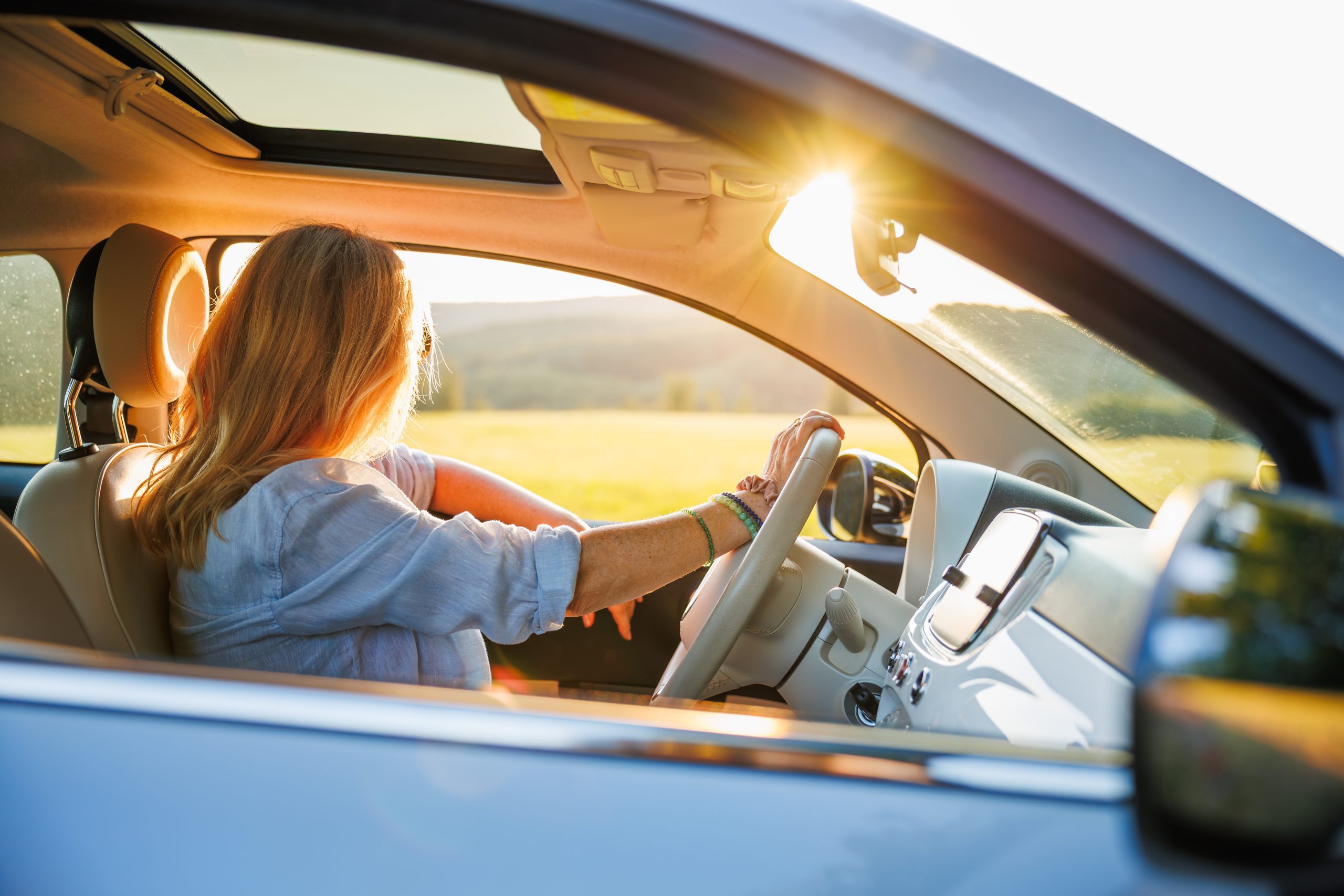Femme au volant de sa voiture par une journée ensoleillée d'été, fenêtre ouverte sur un paysage de campagne